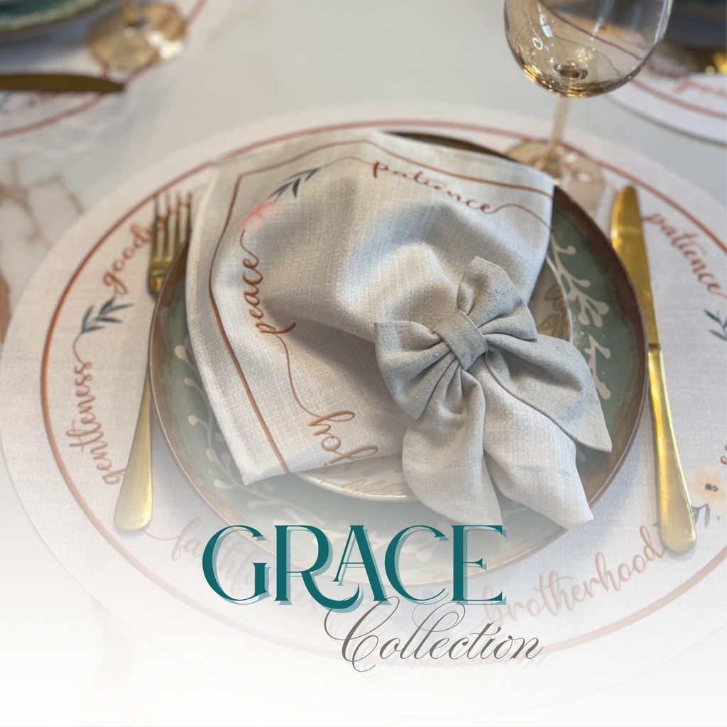 Elegant table setting with a round placemat featuring inspirational words. A folded napkin in a bow shape rests on a plate. Text reads “Grace Collection” with a “Shop Now” button.